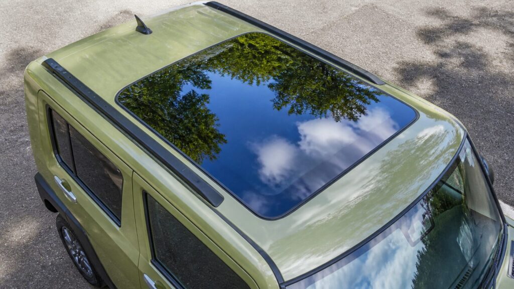Top-down angle of a TAFT roof showing the large fixed square glass panel over the front seats, blue sky and tr